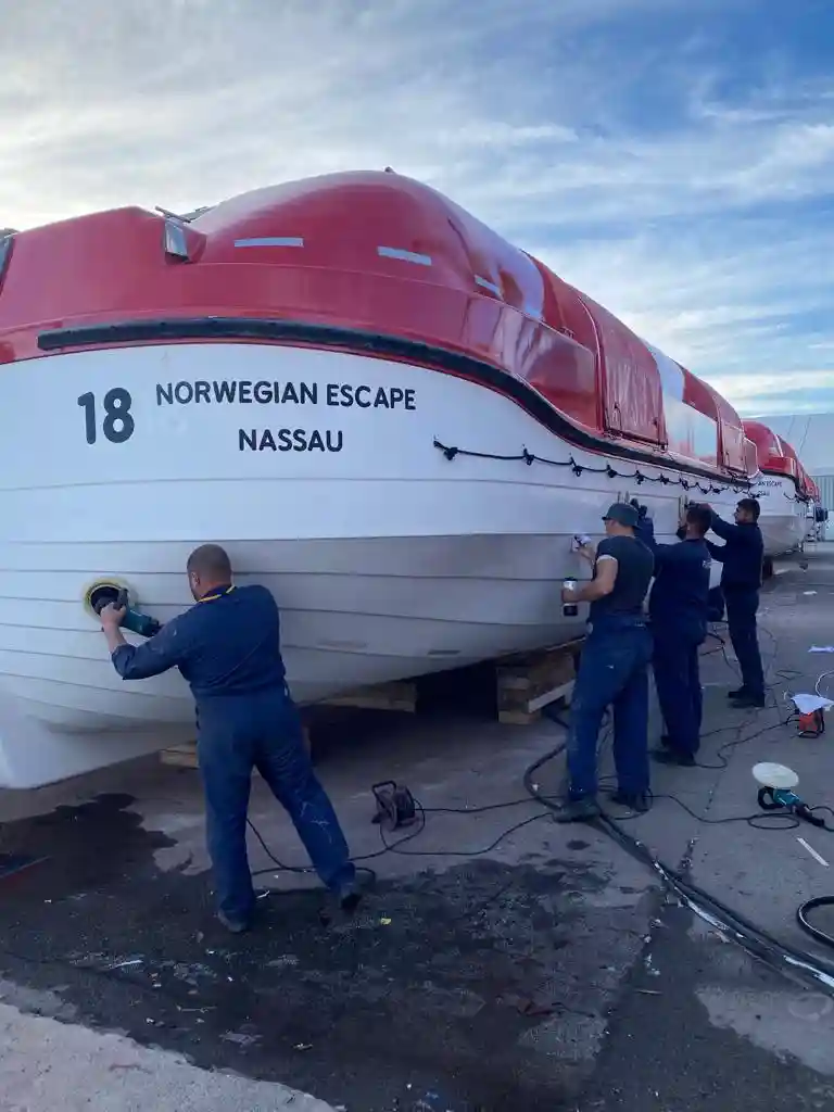 Workers performing maintenance on a lifeboat hull